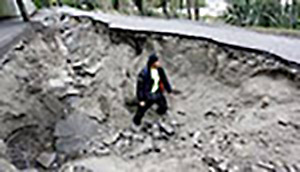 woman stands by collapsed road after Christchurch earthquake